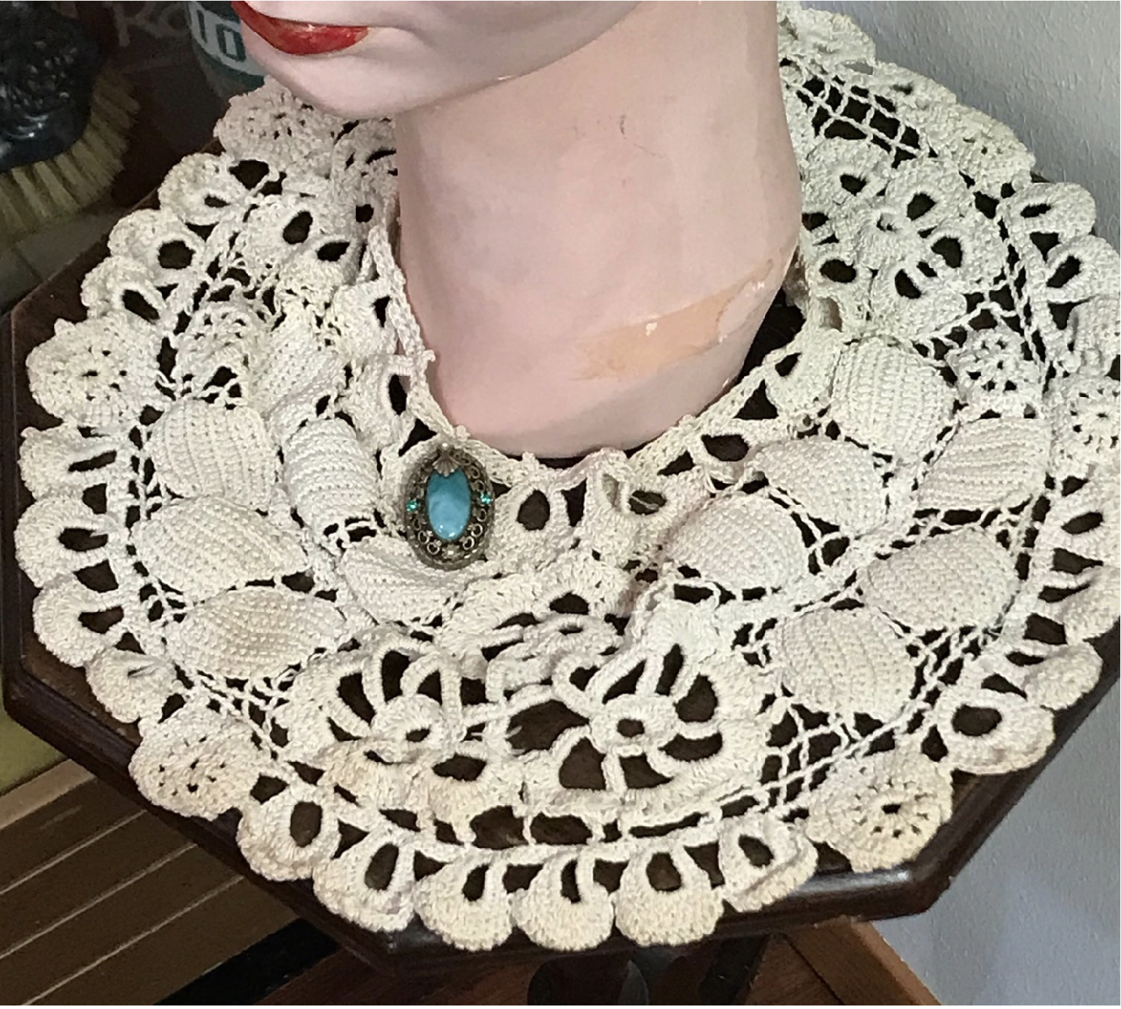 A photograph of a museum display form wearing crocheted collar with a round brooch in the center